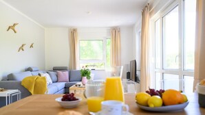 En moderne stue med sofa, sofabord med morgenmad og et stort vindue med gardiner.