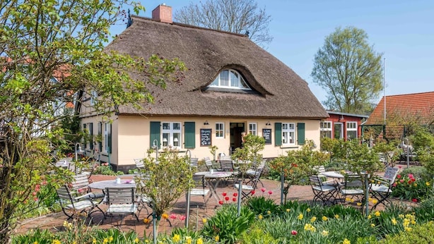 A traditional building with a thatched roof, outdoor seating area with tables and chairs, and a garden with flowers. - Comfortable vacation apartment Residenz am Strand 1-11 in the first row to the Baltic Sea - (Zingst)