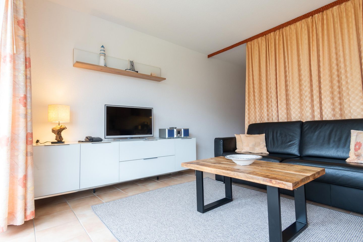 Ein modernes Wohnzimmer mit einem Flachbildfernseher, einem Holztisch, einer schwarzen Couch und einem weißen Schrank.