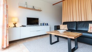 En moderne stue med et fladskærms-tv, et træ sofabord, en sort sofa og et hvidt skab.