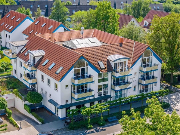 Un hôtel à plusieurs étages, doté d’un toit recouvert de tuiles rouges, de balcons et d’un jardin.