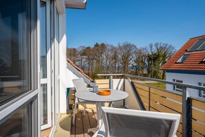 A balcony with a table and chairs, overlooking a residential area with trees and houses.