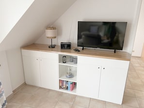 A modern entertainment unit with a flat-screen TV, a radio, and a lamp. - Comfortable vacation apartment in the first row to the Baltic Sea with balcony in Zingst - (Zingst)