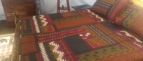 A bed with a colorful quilt, a wooden dresser, and a small statue on top.