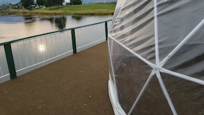Aussicht auf einen Fluss mit einer Brücke, einem grünen Zaun und Bergen im Hintergrund.