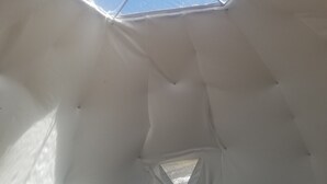 Ein zeltartiges Interieur mit einem geometrischen Oberlicht, einem kleinen Tisch mit einer Skulptur und einem Sessel.