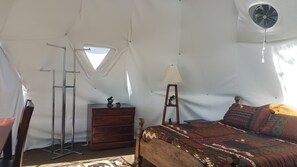 Una habitación con carpa que incluye una cama, un tocador, un espejo y un ventilador.