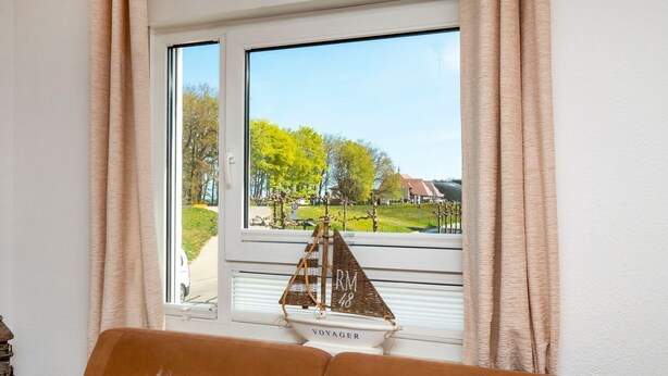 A room with a large window, a wicker boat decoration, and a brown sofa. - Bright, comfortably furnished apartment directly on the dyke and beach - Residence (Zingst)