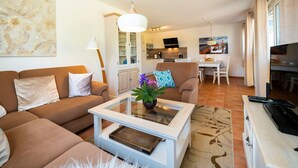 A modern living room with a sofa, coffee table, and a dining area with a table and chairs. - Bright, comfortably furnished apartment directly on the dyke and beach - Residence (Zingst)