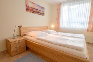 Un dormitorio con cama de madera, mesita de noche con cajones, lámpara y un cuadro en la pared.
