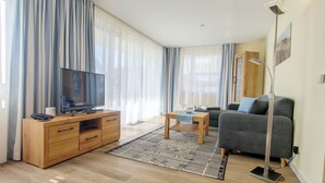 Un salon moderne avec un téléviseur à écran plat, des meubles en bois, un canapé gris et un lampadaire.