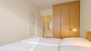 Une chambre avec deux lits, une armoire en bois et une table de chevet avec une lampe.