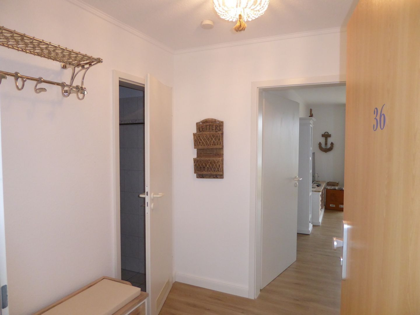 A hallway with a wooden door labeled "36", a coat rack, and a wall-mounted decorative piece.