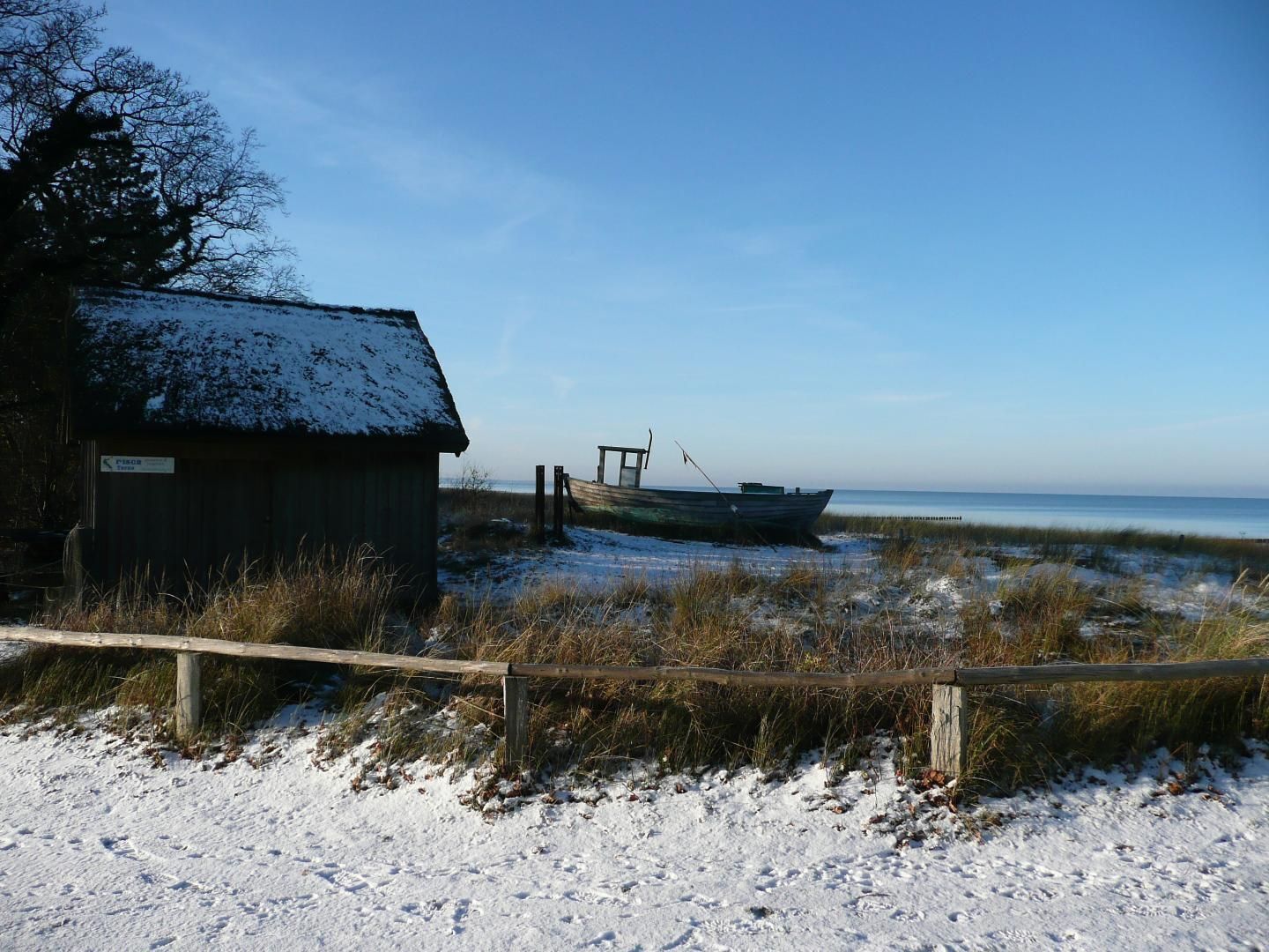 A snow-covered beach with a wooden shack and a boat.