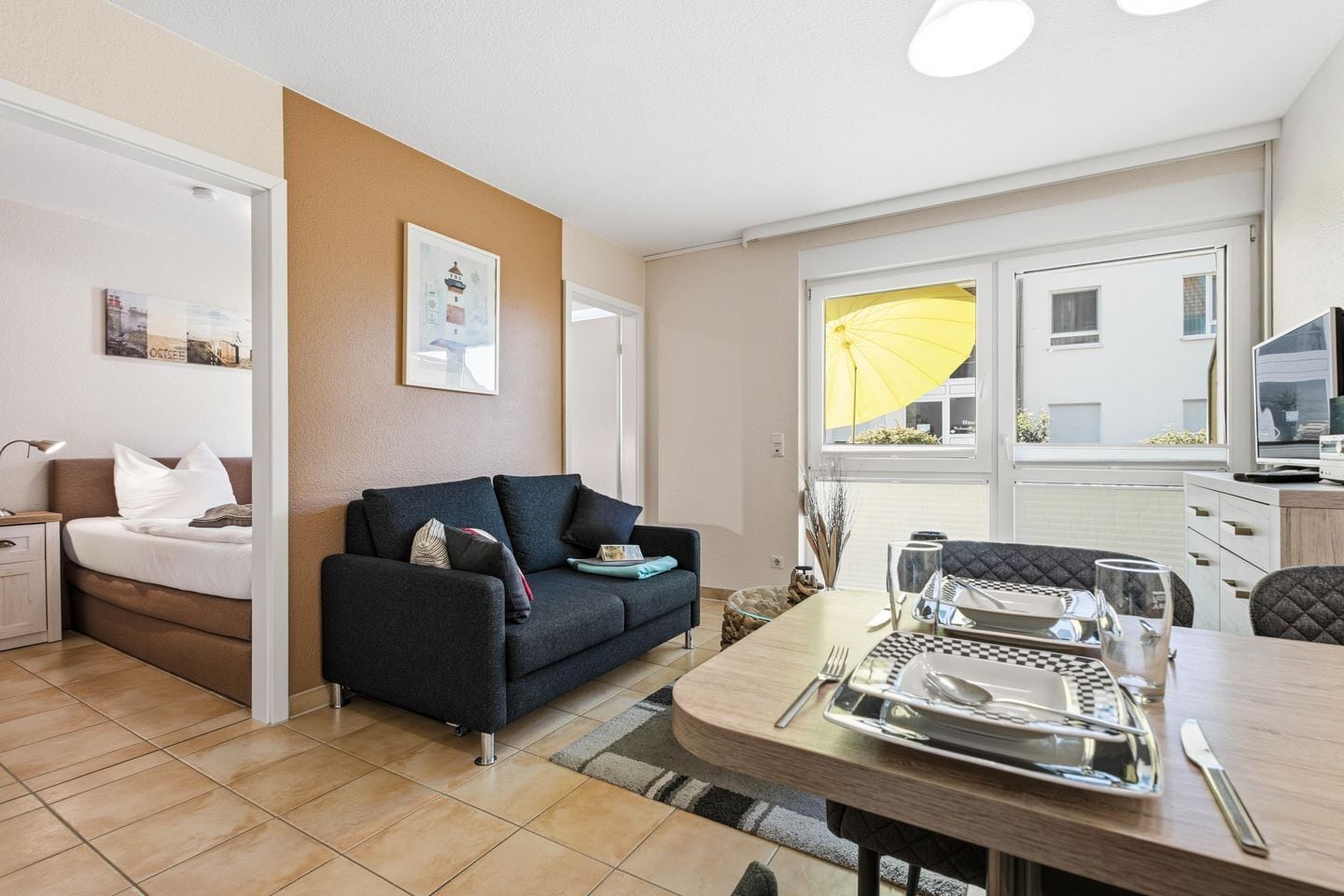 Een moderne woonkamer met een bank, een eettafel gedekt met bestek, en een raam met een gele paraplu.