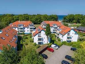 A residential complex with multiple apartment buildings, a parking area, and a view of the sea.