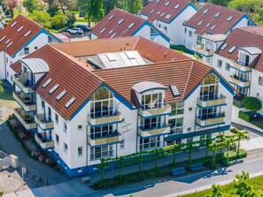 Un immeuble résidentiel moderne à plusieurs étages, doté d’un toit recouvert de tuiles rouges, de balcons et d’une cour intérieure.