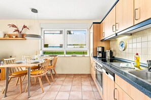 Une cuisine moderne avec des meubles en bois, un coin repas avec des chaises, une fenêtre offrant une belle vue et une machine à café posée sur le plan de travail.