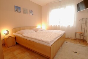 Une chambre à coucher avec un lit en bois, une table de chevet avec une lampe, une chaise et une fenêtre ornée de rideaux légers.