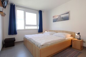 Une chambre à coucher avec un lit en bois, une table de chevet avec une lampe, une fenêtre avec des rideaux et un tableau accroché au mur.