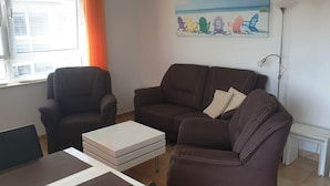 A living room with a brown sofa, a white coffee table, and a window with blinds.