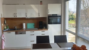 A modern kitchen with white cabinets, a black oven, and a window with blinds.