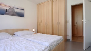 A bedroom with a bed, wooden wardrobe, and a painting of a pier.