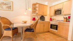 A compact kitchen with a dining area, featuring a round table, wicker chairs, and wooden cabinets.
