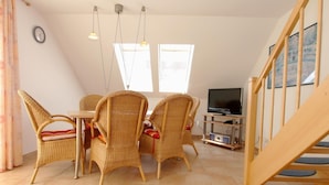 A dining area with wicker chairs and a table, a television on a stand, and a staircase. - Comfortable vacation apartment in the first row on the beach of Zingst with balcony - (Zingst)