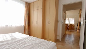 A bedroom with a large bed, wooden wardrobe, and a view of a dining area. - Comfortable vacation apartment in the first row on the beach of Zingst with balcony - (Zingst)