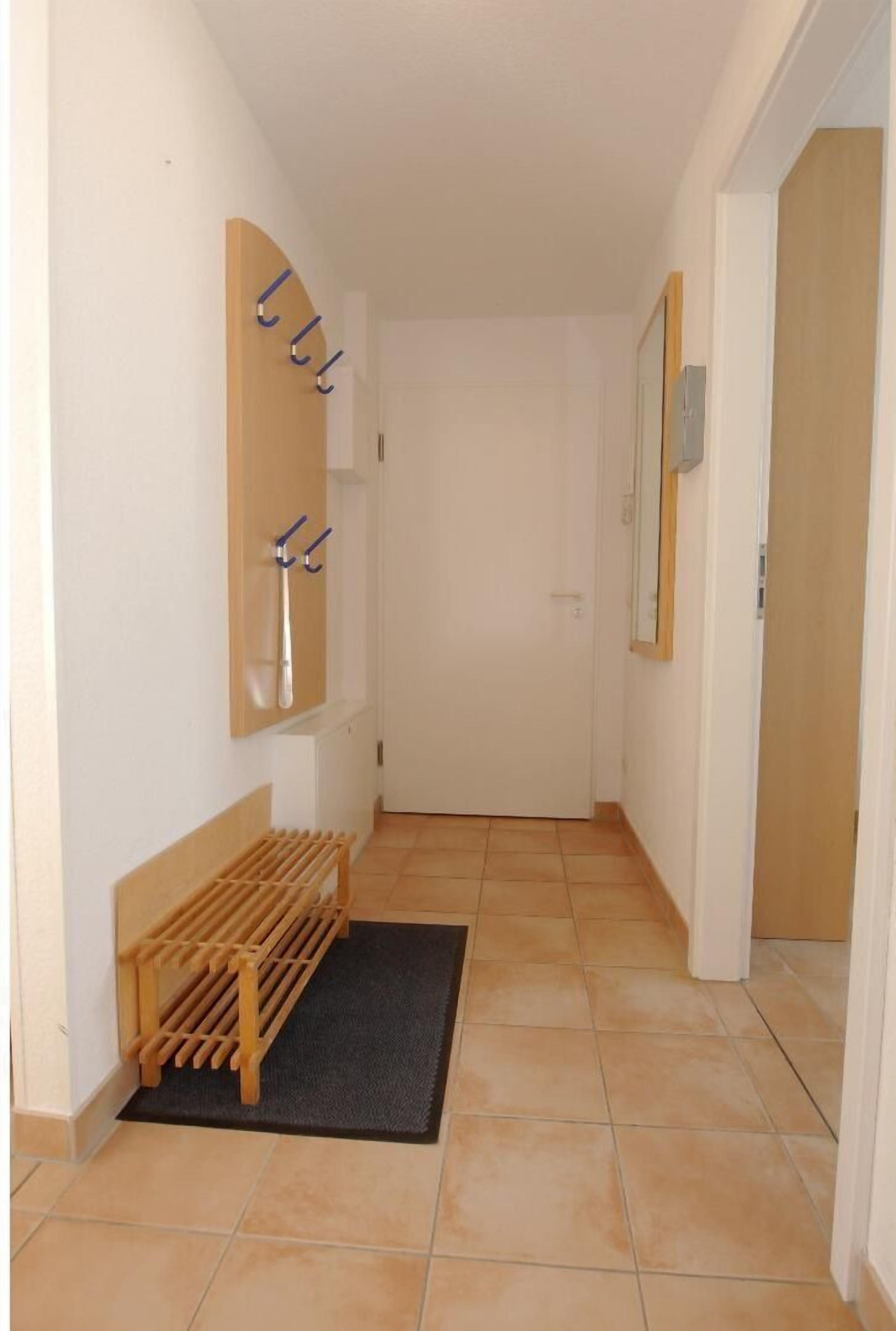 A narrow hallway with a wooden bench, a coat rack, and a mirror on the wall.