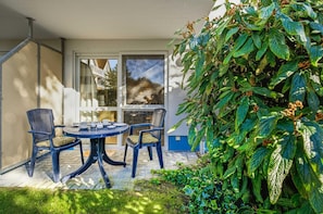 An outdoor patio with a round table and two chairs, surrounded by lush greenery.