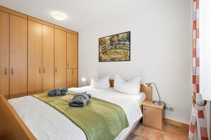 A bedroom with a bed, a nightstand, a lamp, a painting, and wooden wardrobes.