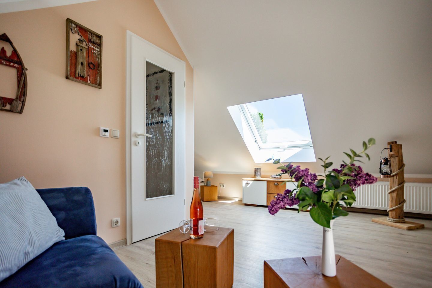 Un apartamento tipo loft moderno con techo inclinado, tragaluces, comedor y sala de estar con un sofá azul y un jarrón de flores.