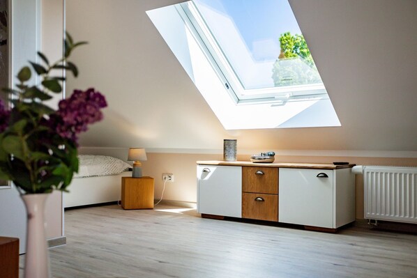 A room with a skylight, a bed, a bedside table with a lamp, a dresser, and a radiator.