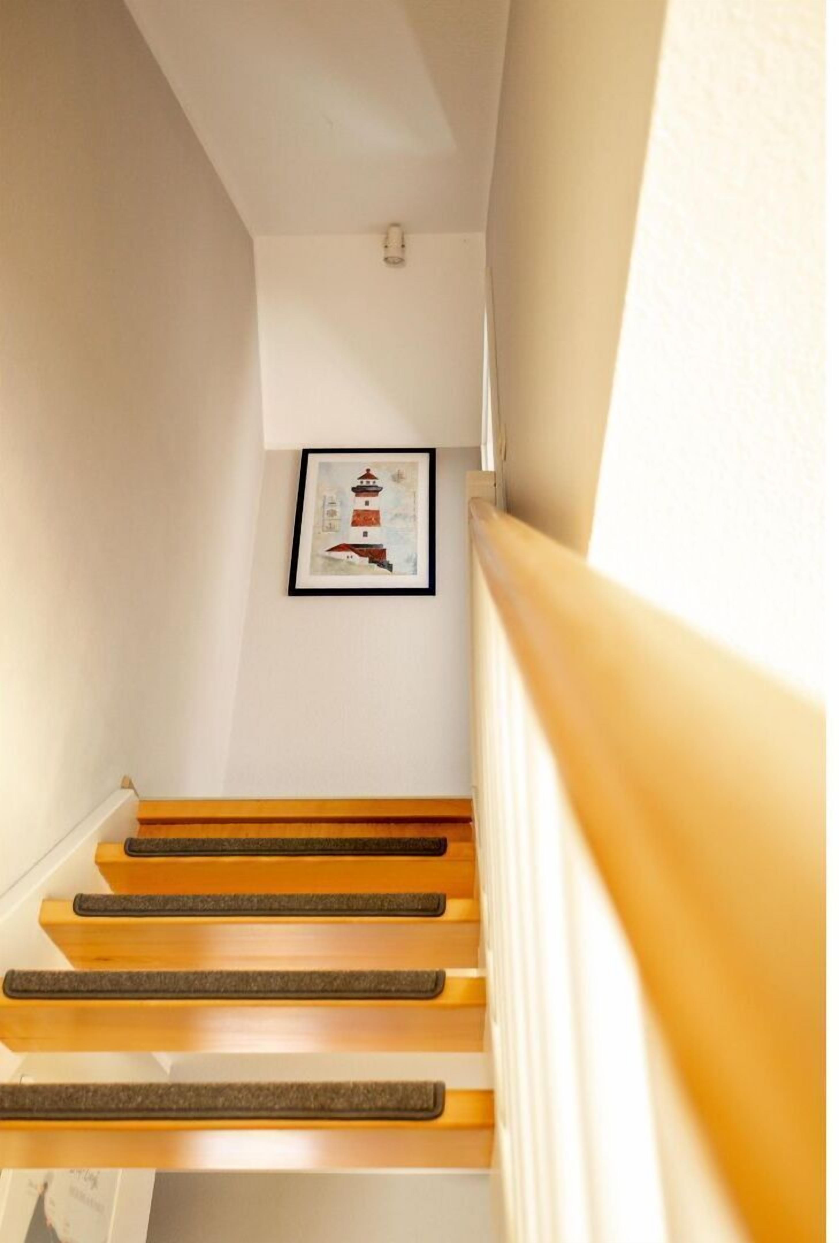 Een trap met houten treden en een leuning, die uitkomt op een plateau met een ingelijste foto.