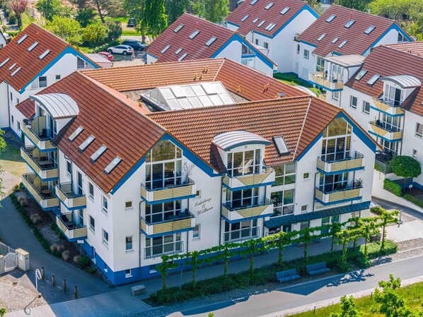 Un moderno edificio residencial de varios pisos, con techo de tejas rojas, balcones y un patio central.