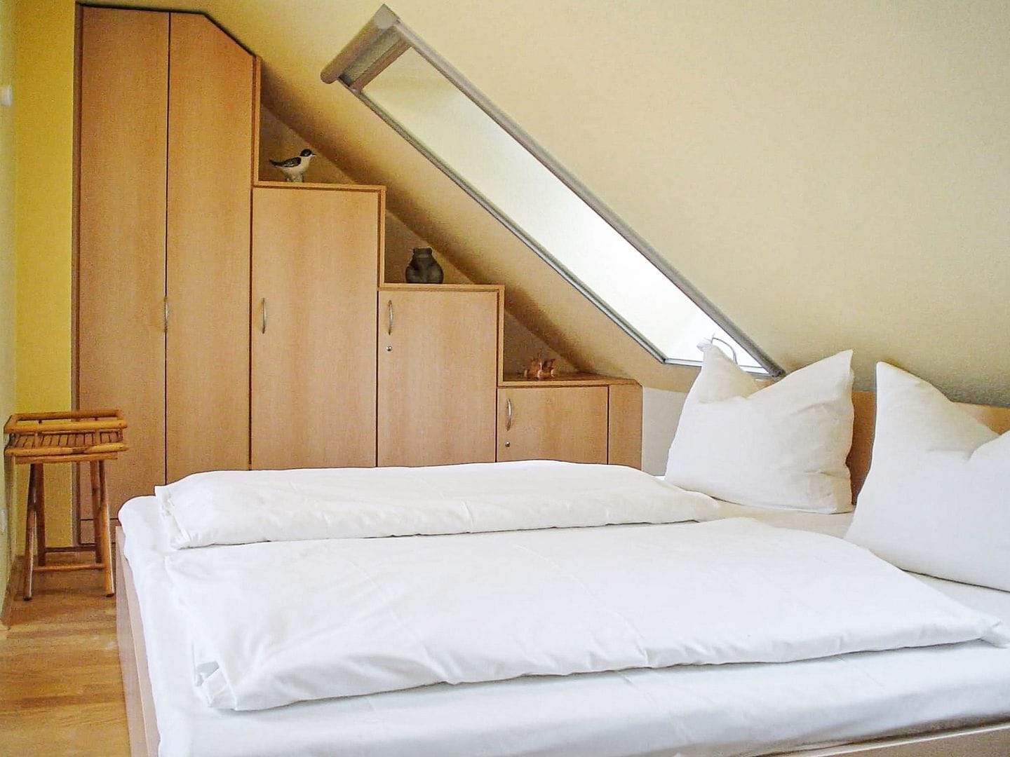 A bedroom with a sloped ceiling, wooden wardrobe, and a bed with white bedding.