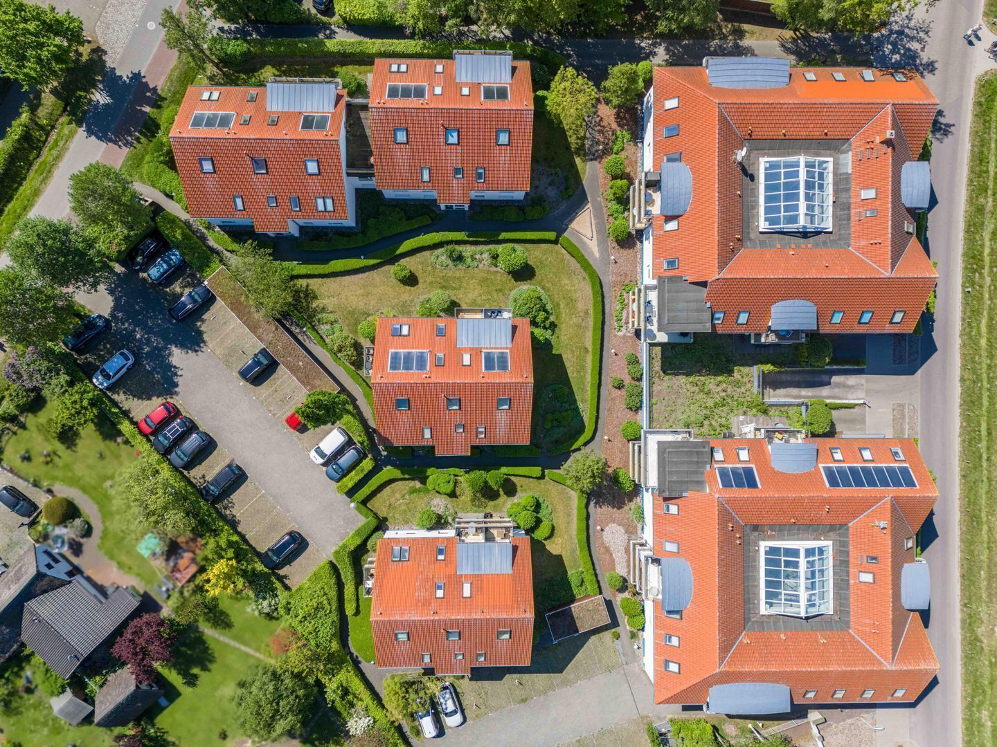 Un complejo residencial con varios edificios de techo rojo, paneles solares y un área de estacionamiento.