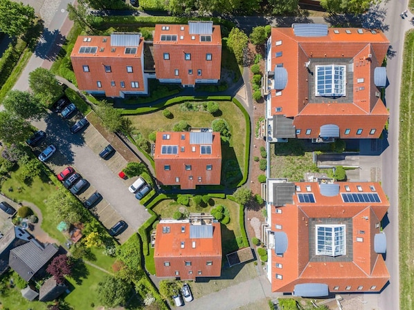A residential complex with multiple red-roofed buildings, solar panels, and a parking area.