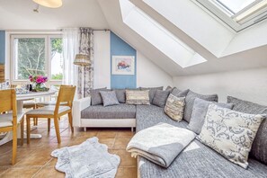 Ein gemütliches Schlafzimmer im Loft-Stil mit großem Dachfenster, einem Essbereich mit Tisch und Stühlen sowie einer Wohnbereits mit Sofa und Zierkissen.