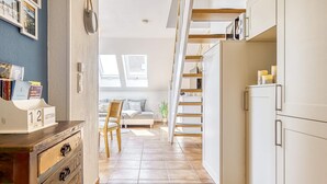 Una cocina compacta con armarios blancos, una silla de madera y una cama al fondo.