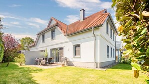 Ein zweistöckiges Haus mit rotem Ziegeldach, einer überdachten Terrasse mit Gartenmöbeln und einem gepflegten Rasen.