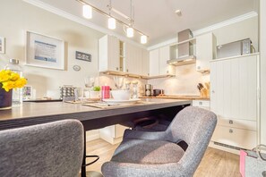 Une cuisine moderne avec des meubles blancs, une table à manger avec des chaises et un luminaire suspendu.