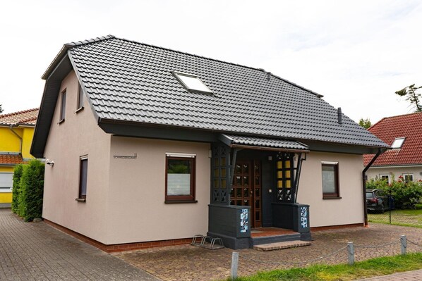 Une maison à deux étages, avec un toit en tuiles, un porche à l’avant et un petit jardin.