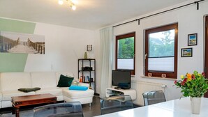 A modern living room with a white sofa, a coffee table, a TV, and a dining area with a table and chairs.