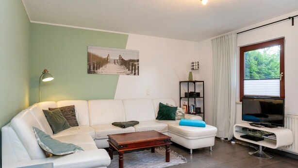 A modern living room with a white sofa, a wooden coffee table, a bookshelf, and a television.