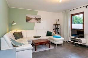 A modern living room with a white sofa, a wooden coffee table, a bookshelf, and a television. - Haus Zeitlos - Beautiful detached vacation home with furnished south-facing terrace and (Zingst)