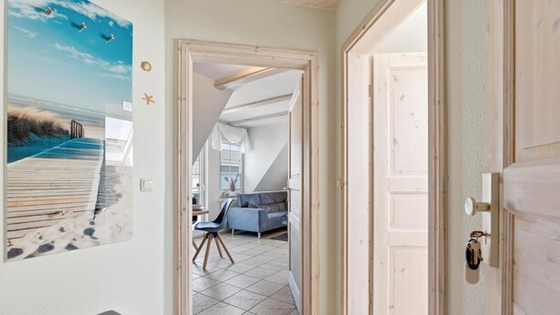 Un couloir menant à un espace de vie avec vue sur l’extérieur, une porte dotée d’un trou de serrure et un tableau accroché au mur.