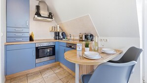 Une cuisine compacte avec des meubles bleus, un four encastré, une machine à café et un coin repas comprenant une table et des chaises.